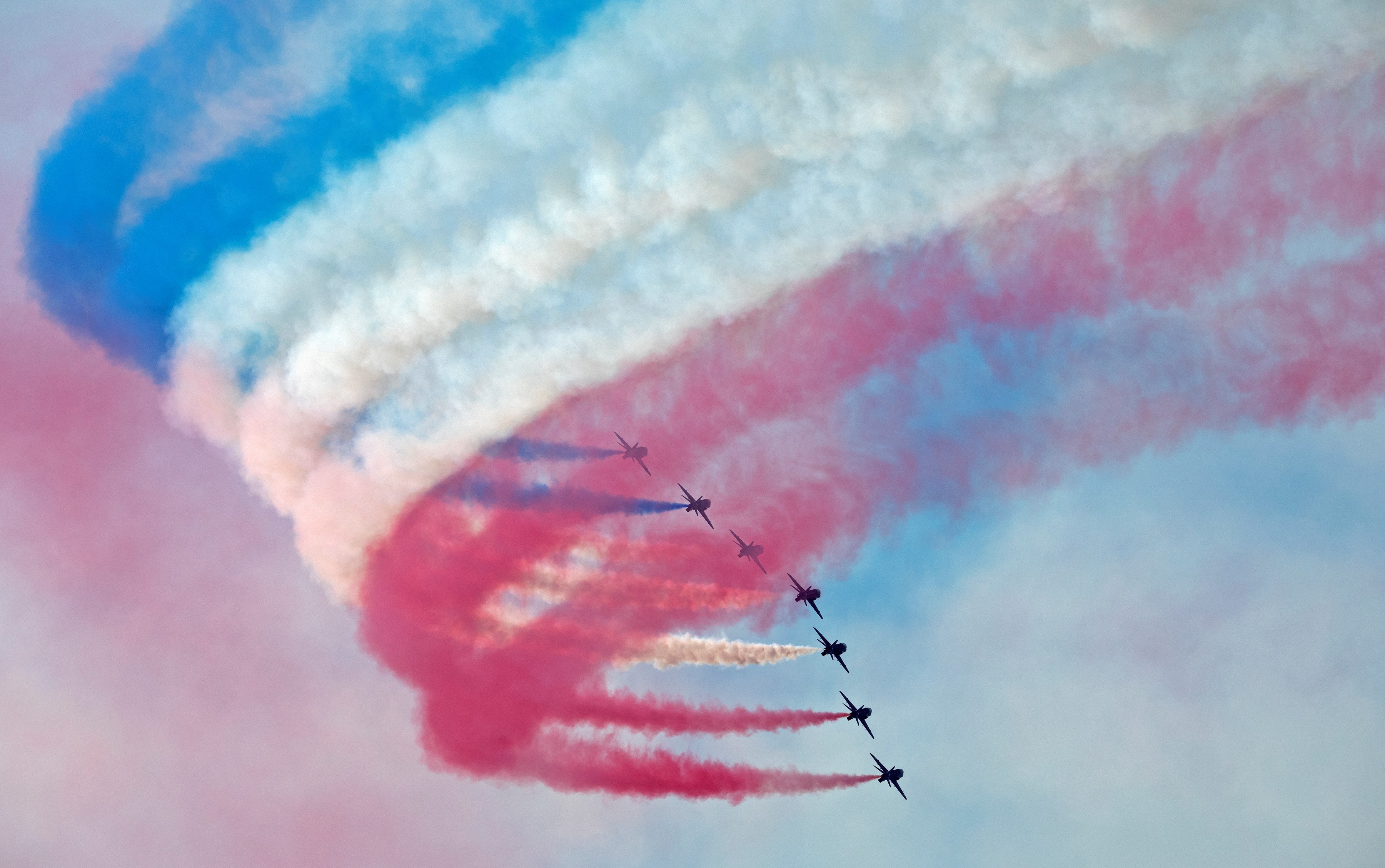 Image shows the Red Arrows performing with red, blue and white smoke trails.